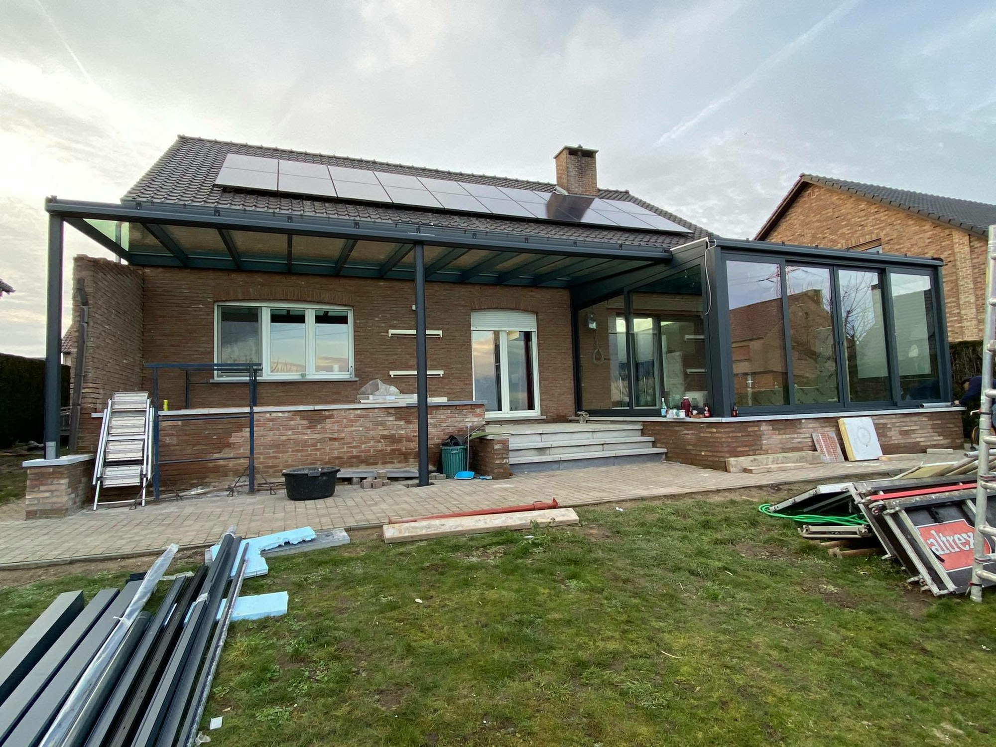 Véranda à toiture vitrée sous panneaux solaires en cours de finition
