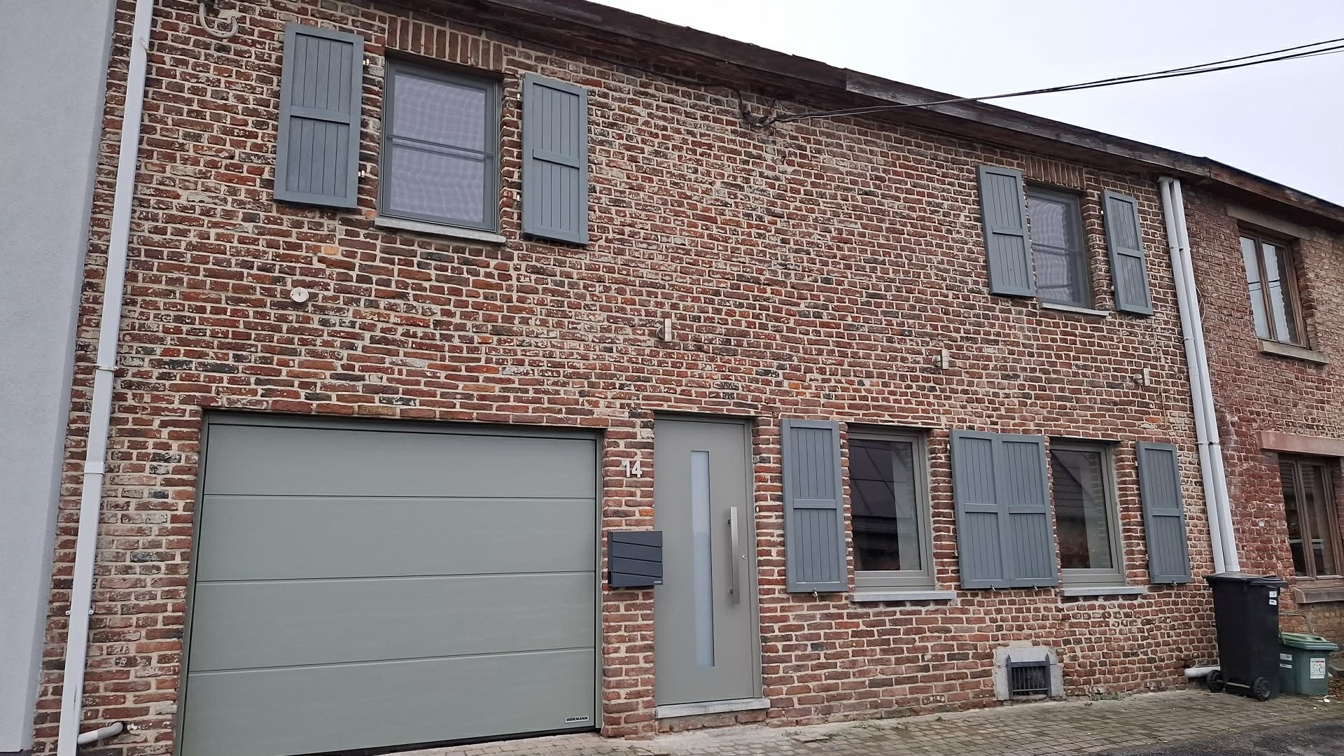 Maison en brique avec porte de garage sectionnelle et volets gris